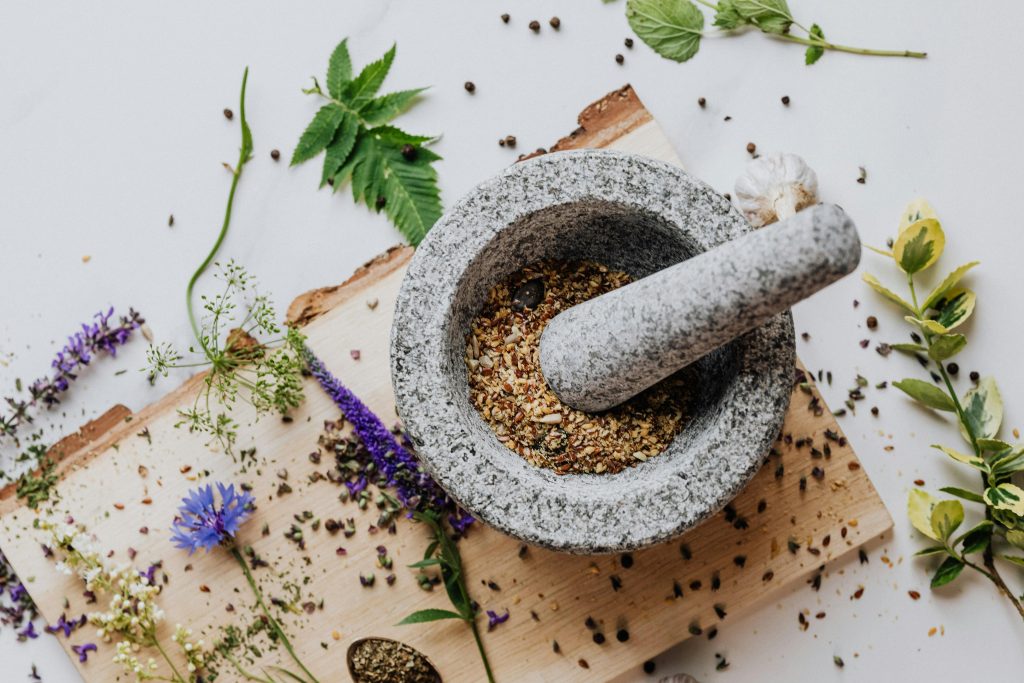 A stone mortar and pestle with herbs and leaves scattered on a wooden board, perfect for culinary and herbal imagery.